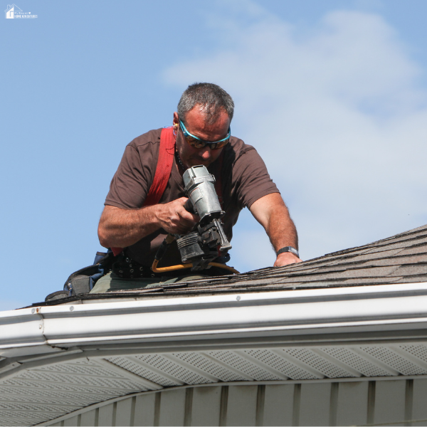 A contractor uses a nail gun while repairing shingles on a residential roof, showing how routine roof maintenance protects a home’s value.