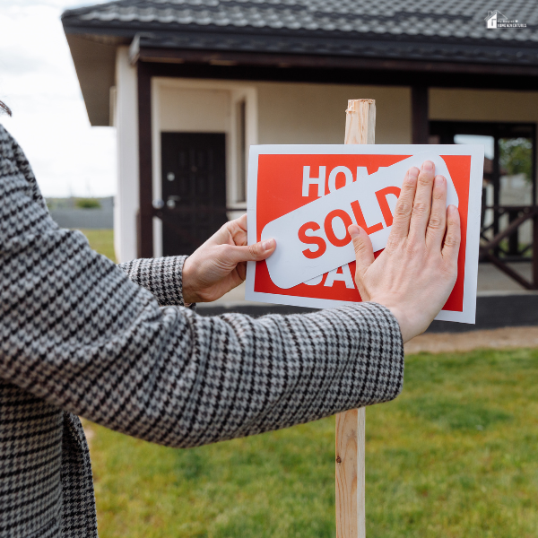 A homeowner places a sold sticker on a real estate sign in front of a house, highlighting how good roof maintenance can lead to a higher resale value.