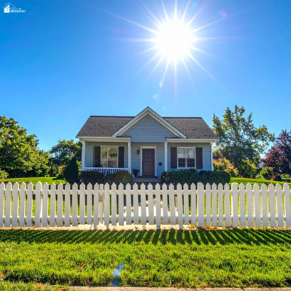 A small blue house with a white picket fence and bright sunshine in a clear blue sky, showcasing curb appeal and fencing style.