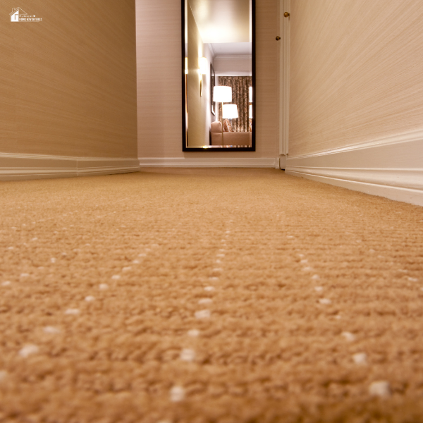 A view down a hallway with a textured carpet leading to a well-lit room in the background.