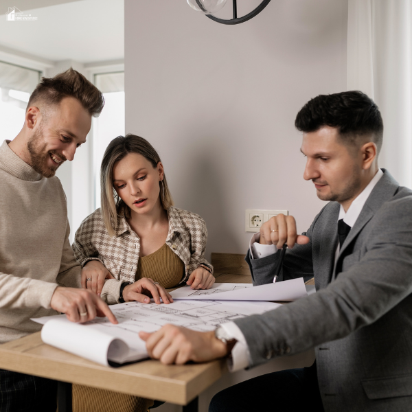 Two men and a woman reviewing a floor plan together at a table, indicating a real estate discussion or property planning meeting.
