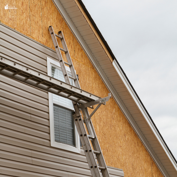 Home steel siding installation in progress with ladders and partially covered exterior wall.