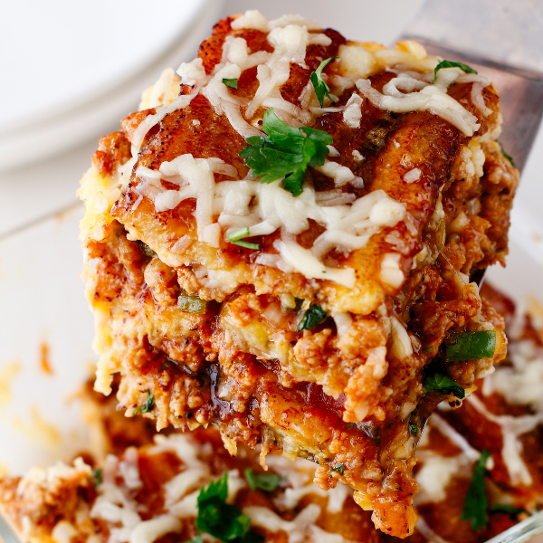 A thick, cheesy slice of pastelón being served, revealing its hearty meat and plantain layers.