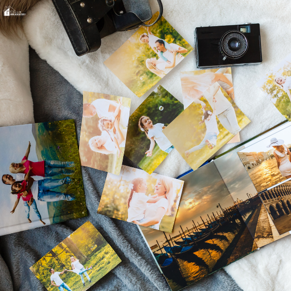 Printed photos and open photo books are spread out on a blanket with a vintage camera nearby.