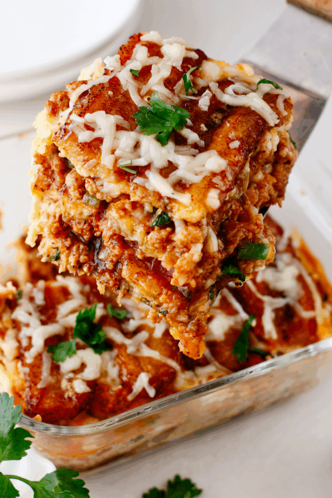 A thick, cheesy slice of pastelón being served, revealing its hearty meat and plantain layers.