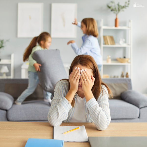 A mom covers her face in frustration while kids play loudly behind her, showing the need for budget-friendly ways to calm a noisy home.