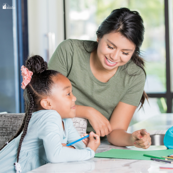 An au pair assisting a young girl with homework at the table, offering support with learning and daily tasks.