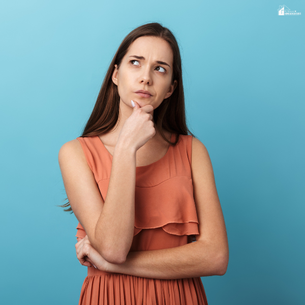 A woman stands with her hand on her chin and a thoughtful expression, representing mindful thinking before spending during financially cautious times.