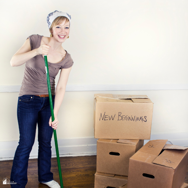 A smiling woman stands with moving boxes labeled "New Beginnings," ready to start fresh after selling her home.