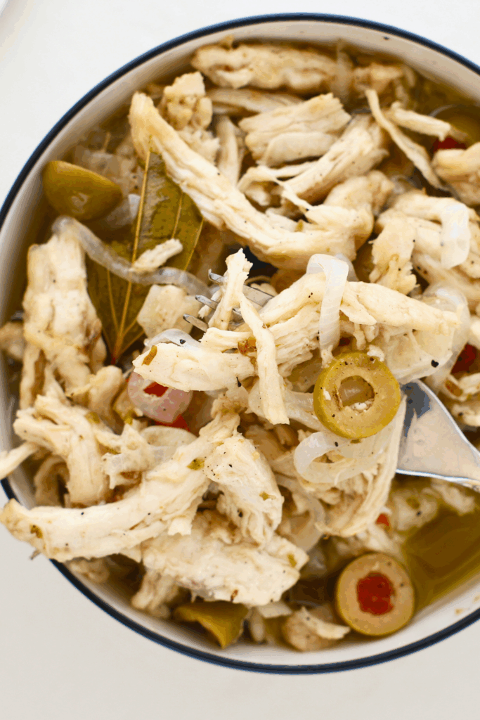 Close-up of pollo en escabeche with shredded vinegar marinated chicken, onions, green olives, bay leaves, and spices in a bowl, a classic Puerto Rican chicken recipe served at room temperature