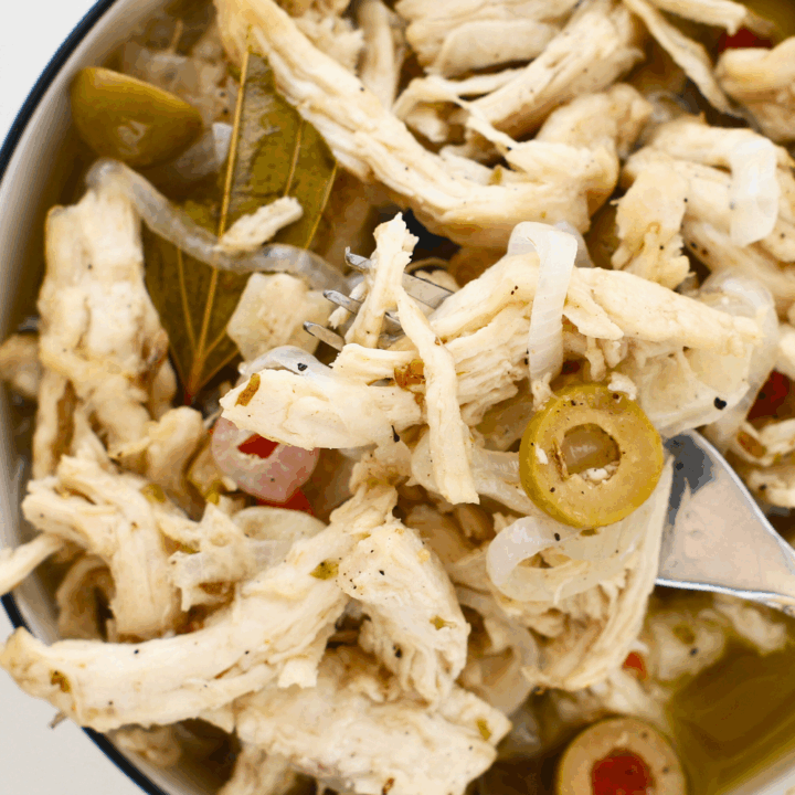 Close-up of pollo en escabeche with shredded vinegar marinated chicken, onions, green olives, bay leaves, and spices in a bowl, a classic Puerto Rican chicken recipe served at room temperature