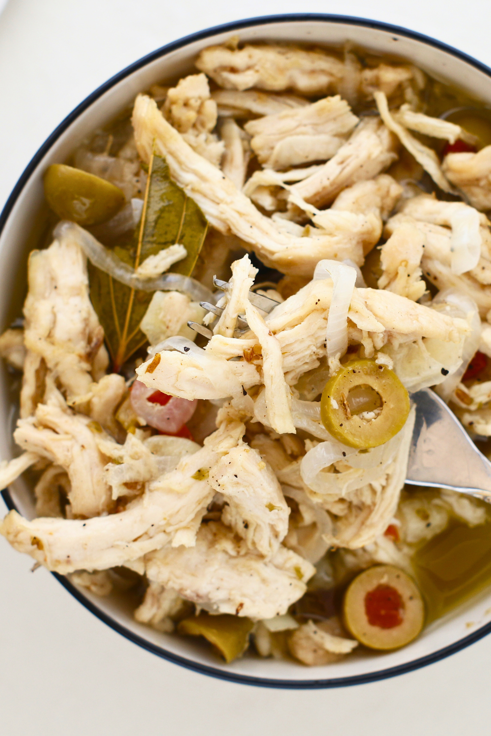 Close-up of pollo en escabeche with shredded vinegar marinated chicken, onions, green olives, bay leaves, and spices in a bowl, a classic Puerto Rican chicken recipe served at room temperature