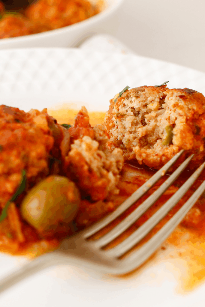 Close-up of a Puerto Rican meatball cut open to show the tender inside, simmered in tomato sauce with olives, also known as albondigas guisadas