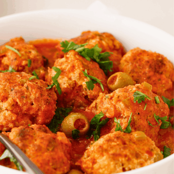 Puerto Rican meatballs simmered in a savory tomato sauce with sofrito, sazon, and green olives, known as albondigas guisadas, garnished with fresh cilantro in a serving bowl