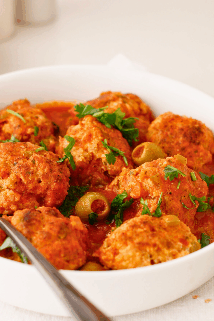 Puerto Rican meatballs simmered in a savory tomato sauce with sofrito, sazon, and green olives, known as albondigas guisadas, garnished with fresh cilantro in a serving bowl