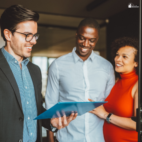A couple smiles while reviewing documents with a real estate agent, representing important discussions during the home-selling process.