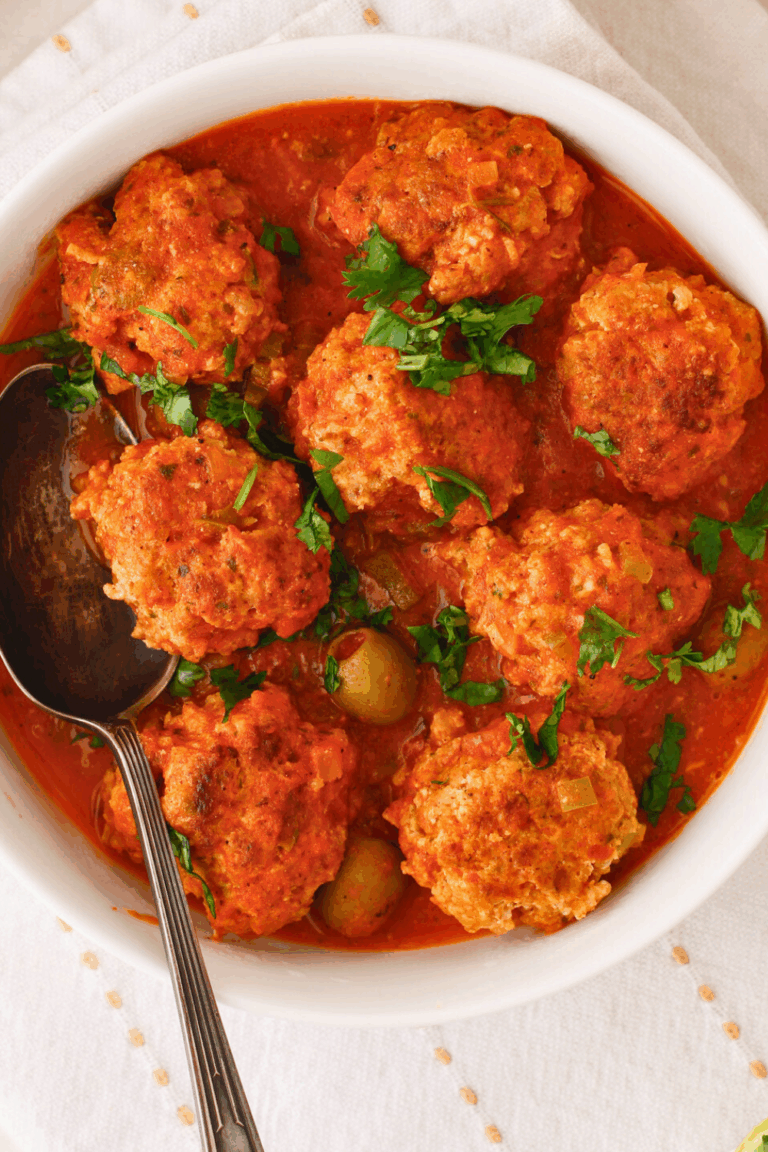 Puerto Rican meatballs simmered in a rich tomato sauce with sofrito, sazon, and green olives, also known as albondigas guisadas, garnished with fresh cilantro in a serving bowl