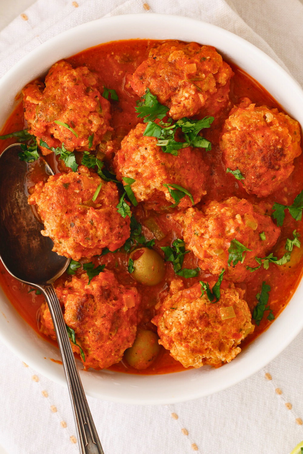 Puerto Rican meatballs simmered in a rich tomato sauce with sofrito, sazon, and green olives, also known as albondigas guisadas, garnished with fresh cilantro in a serving bowl
