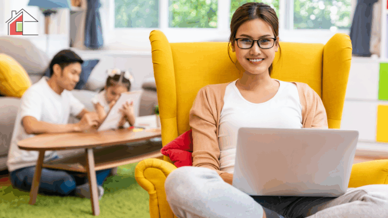 A working mom using a laptop from home while her family spends time together in the background, showing a realistic work from home setup for working moms building flexible businesses and balancing income with family life.