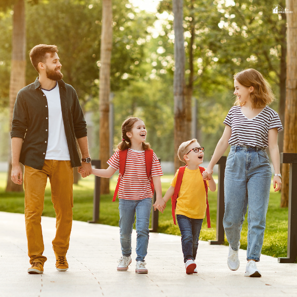 Parents walking with their children outdoors on a sunny path, symbolizing simple local adventures as part of a creative stay-at-home getaway.