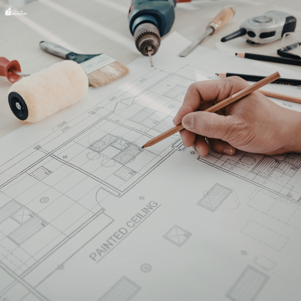 A person drafts renovation plans on a construction blueprint, showing how careful planning helps avoid costly remodeling errors.