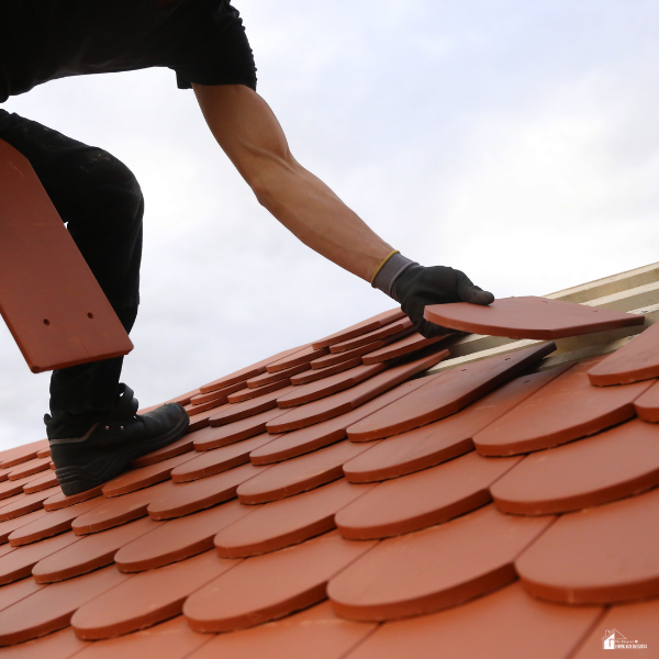 Roofer installing red clay tiles on a sloped roof, illustrating material selection, durability, and installation considerations.