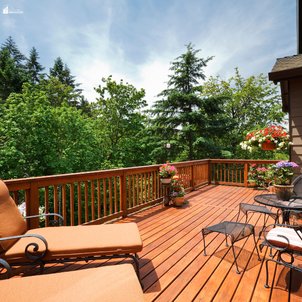 Spacious wooden deck with lounge chairs, patio dining set, railing planters, and lush green tree views creating a relaxing outdoor retreat.