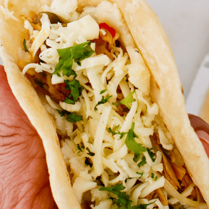 Close-up of Puerto Rican chicken tacos with mashed potatoes, shredded chicken, melted cheese, and fresh cilantro inside a soft tortilla.