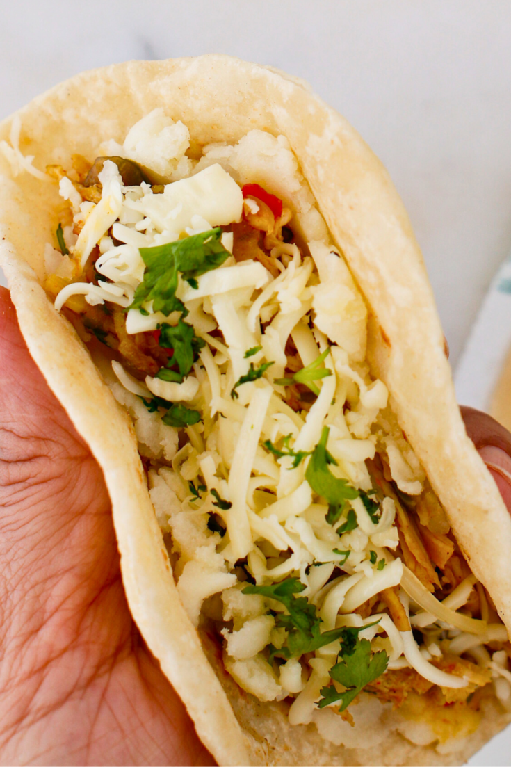 Close-up of Puerto Rican chicken tacos with mashed potatoes, shredded chicken, melted cheese, and fresh cilantro inside a soft tortilla.
