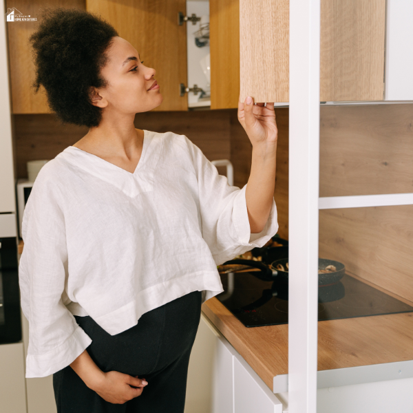 A woman inspects an upper RTA cabinet in a compact kitchen with wood tones, demonstrating functional and affordable storage improvements.