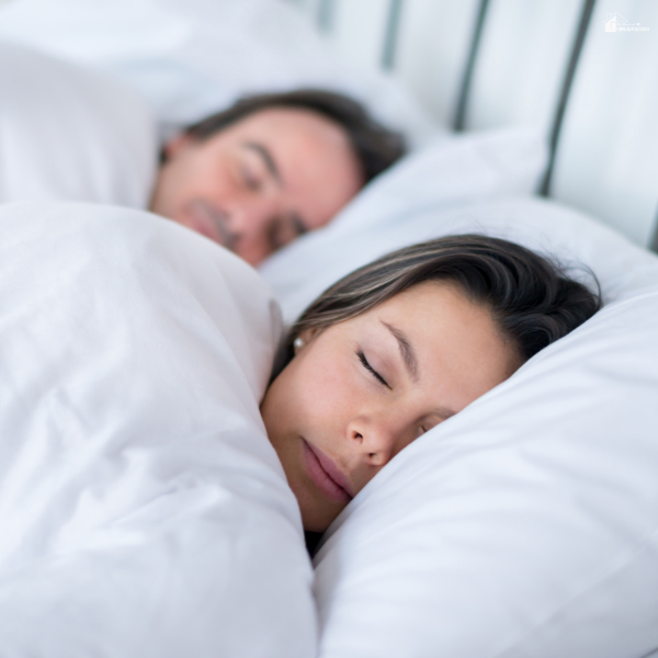 Couple sleeping peacefully in bed under soft bedding, representing the importance of restful sleep for parents managing daily responsibilities at home.