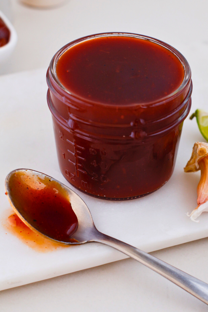 Homemade Puerto Rican guava BBQ sauce in a glass jar with spoon, sweet and tangy Caribbean barbecue sauce made with guava paste, perfect glaze for grilled chicken, pork, ribs, and pinchos