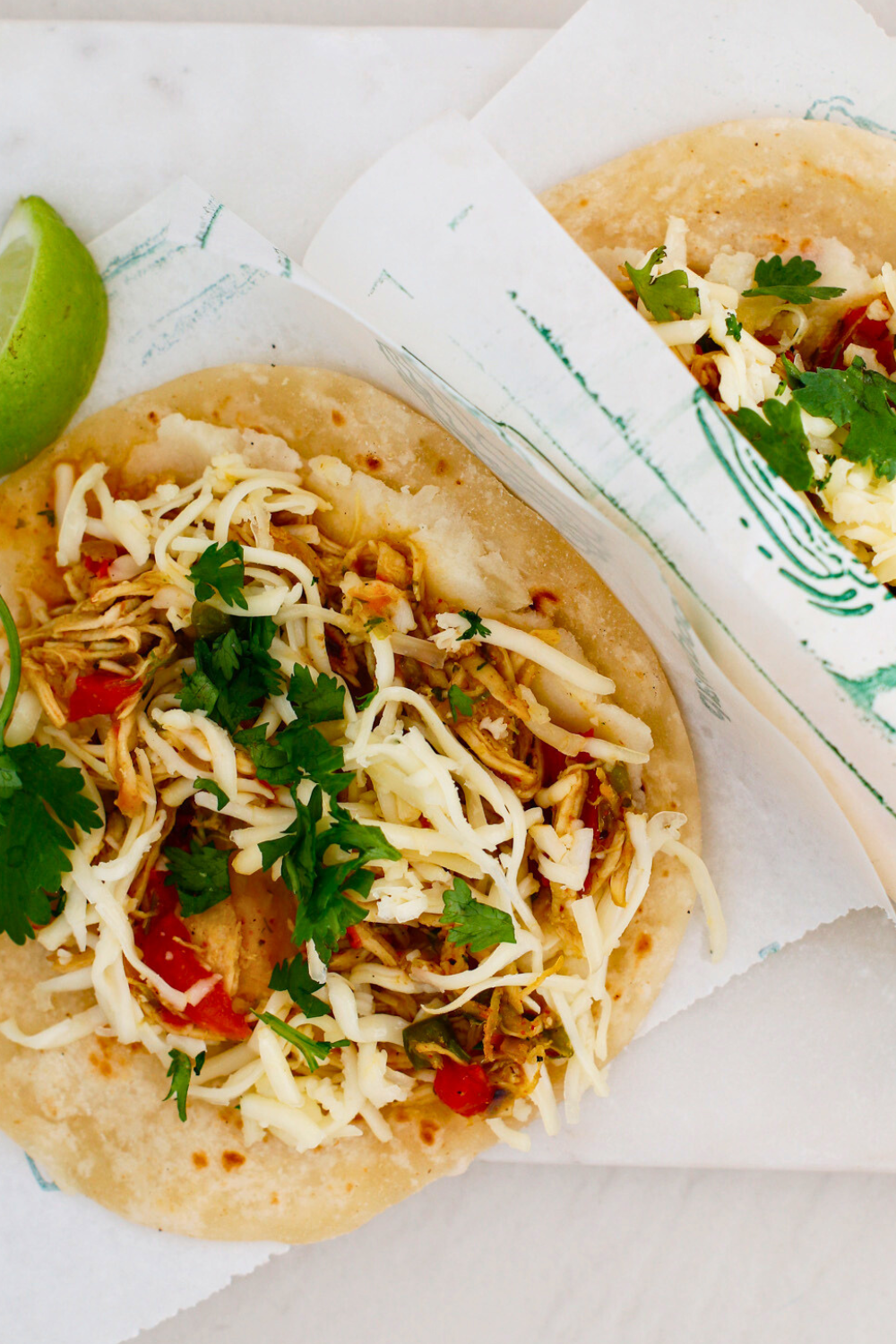 Puerto Rican chicken tacos with mashed potatoes topped with shredded chicken, melted cheese, red and green peppers, fresh cilantro, and lime on soft tortillas.