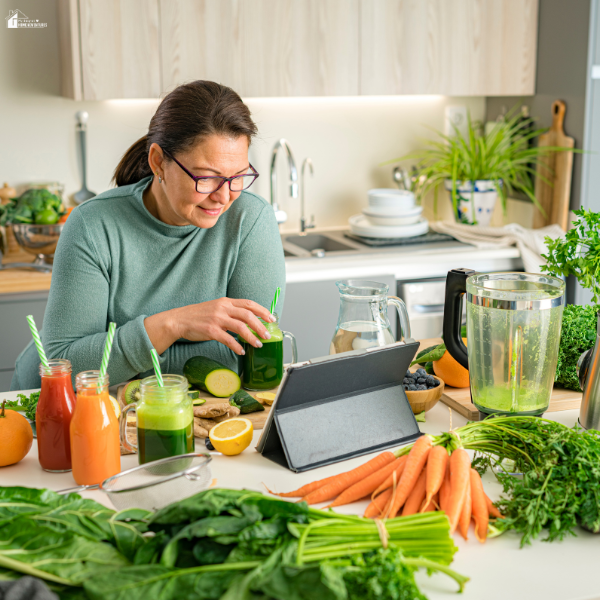 Woman preparing healthy drinks in a kitchen while using a tablet, representing managing work responsibilities alongside home projects.