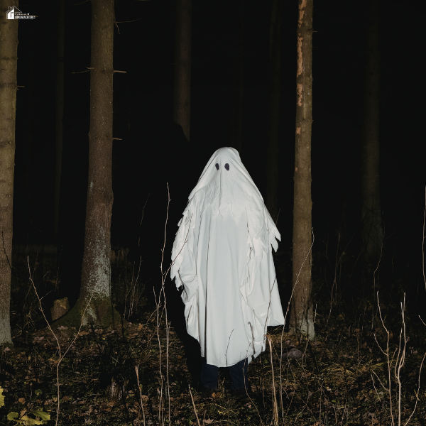Figure dressed as a ghost standing in a dark forest at night, symbolizing eerie legends and paranormal stories shared during nighttime walking experiences.