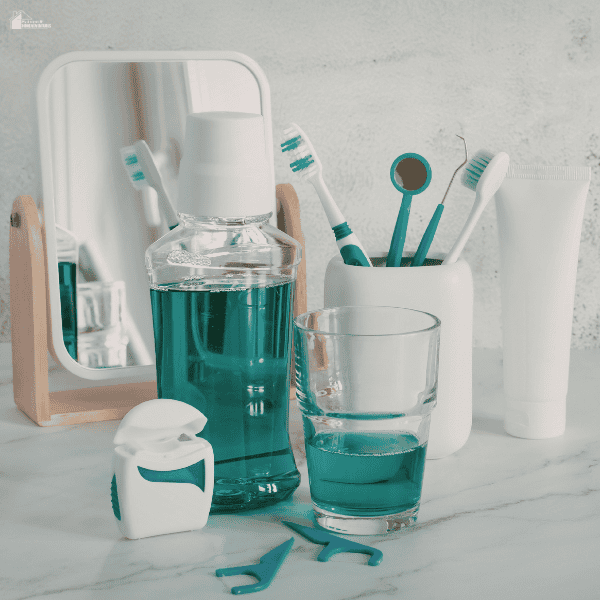 Bathroom countertop setup with toothbrushes, mouthwash, dental floss, and hygiene items neatly arranged beside a small mirror.
