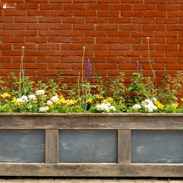 Raised stainless steel planters filled with colorful flowers set against a brick wall, showing a neat and low-maintenance garden design.