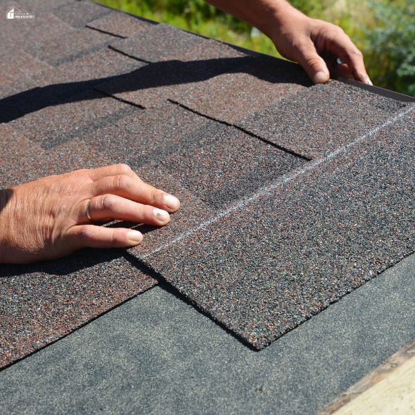 Close-up of hands positioning asphalt shingles during a residential roof installation to improve durability and weather protection.
