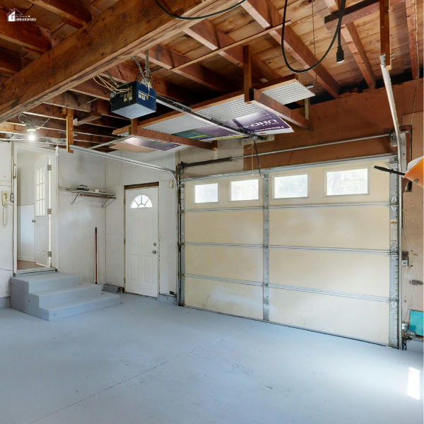 Empty garage interior with exposed beams and door, showing potential for transforming into a functional business workspace.