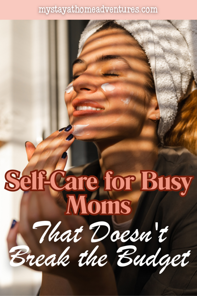 Woman with a towel wrapped around her hair applying face moisturizer during a calm and inexpensive self-care moment for busy moms at home.