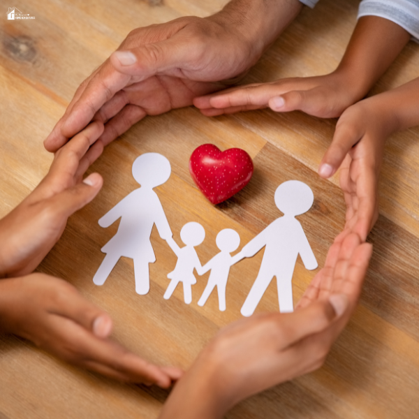 Hands forming a protective circle around paper cutouts of a family and a small heart, symbolizing safety, care, and protecting loved ones at home.