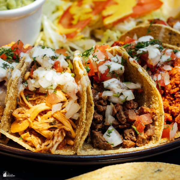 Plate of street-style tacos with shredded chicken, seasoned beef, and chorizo topped with onions and tomatoes as part of a collection of the best Cinco de Mayo recipes.