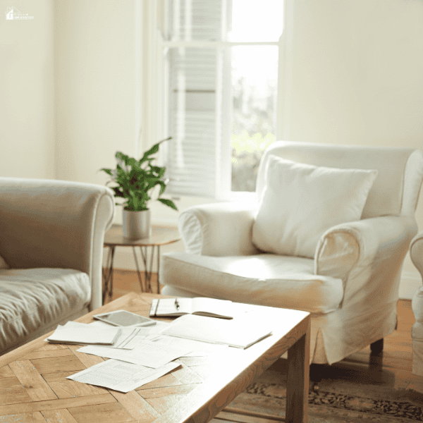 Living room with scattered papers and items on a table, showing the need for routine home maintenance and organization to reduce clutter.