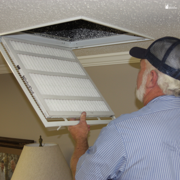 Person replacing an air filter in a ceiling vent to improve airflow and maintain a well-functioning home.