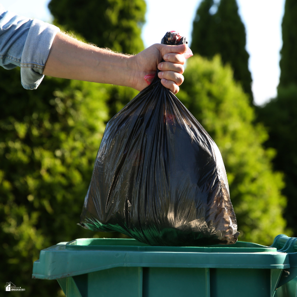 Person placing a garbage bag into a wheeled trash container, showing the convenience of using mobile trash receptacles at home.