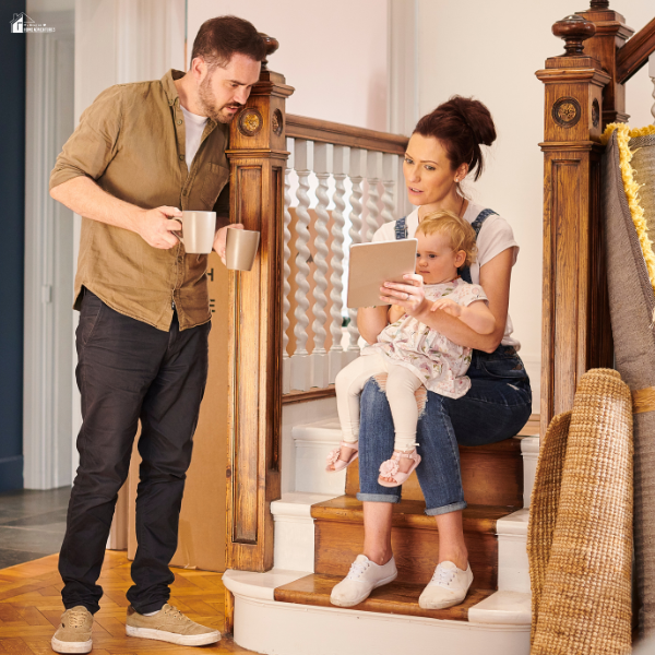 Parent sitting on stairs with a child while checking a tablet and holding coffee, showing small home habits that save time and money in daily routines.