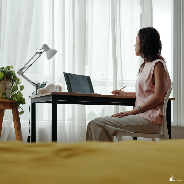 Person sitting at a desk with a laptop and notebook near a window, showing small daily habits that help reduce chaos at home.