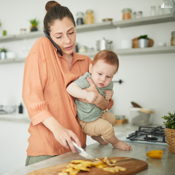 Parent holding a baby while preparing food and talking on the phone, showing the unseen tasks of keeping a home running.