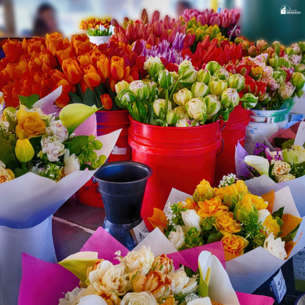 Colorful buckets of fresh flowers arranged in a market setting, showing a wide variety of blooms available in bulk.