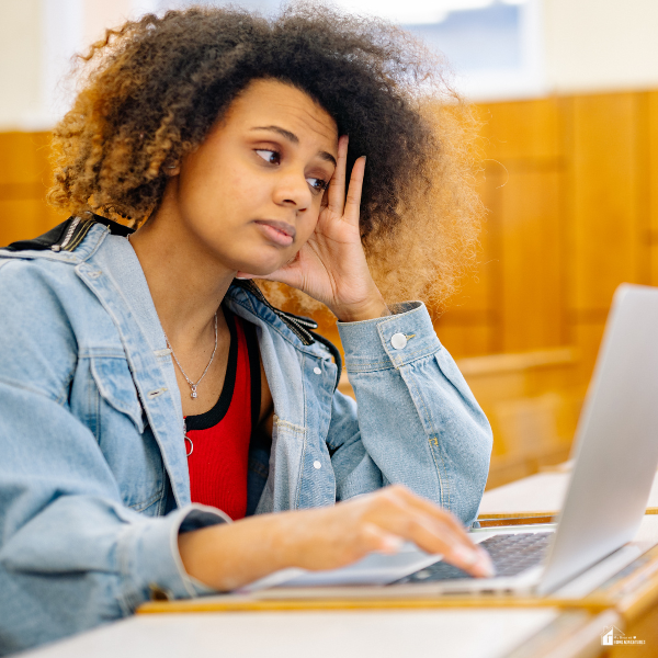 College student looking stressed while working on a laptop, representing financial concerns about paying for school and managing education costs.